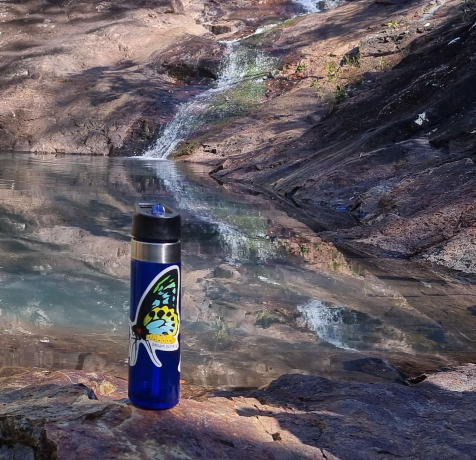 Waterbottle with awesome butterfly sticker in front of a waterfall